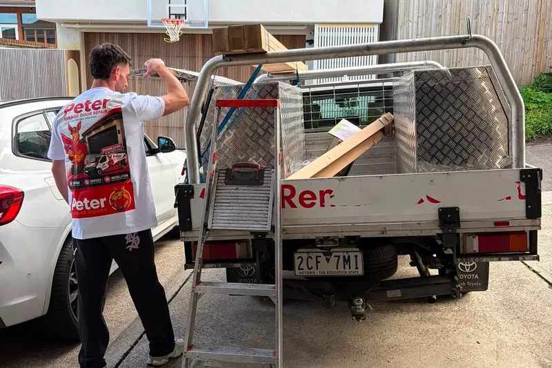 Peter Garage Doors technician in branded uniform loading garage door parts onto the work ute before a repair job