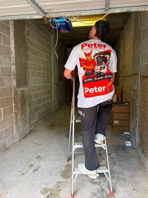 Peter Garage Doors technician on a ladder installing a garage door opener motor in a Perth home garage